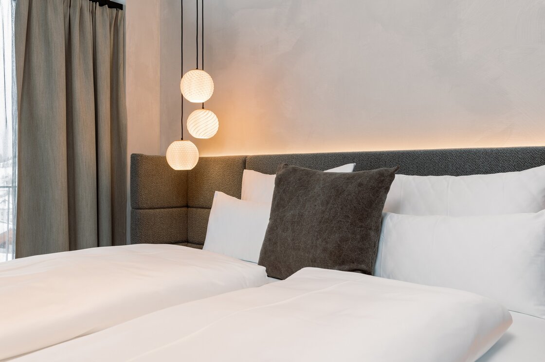 Schlafzimmer im Penthouse mit weichem Licht Ein modern gestaltetes Schlafzimmer mit großem Bett, Kissen und drei hängenden Leuchten neben Vorhängen.