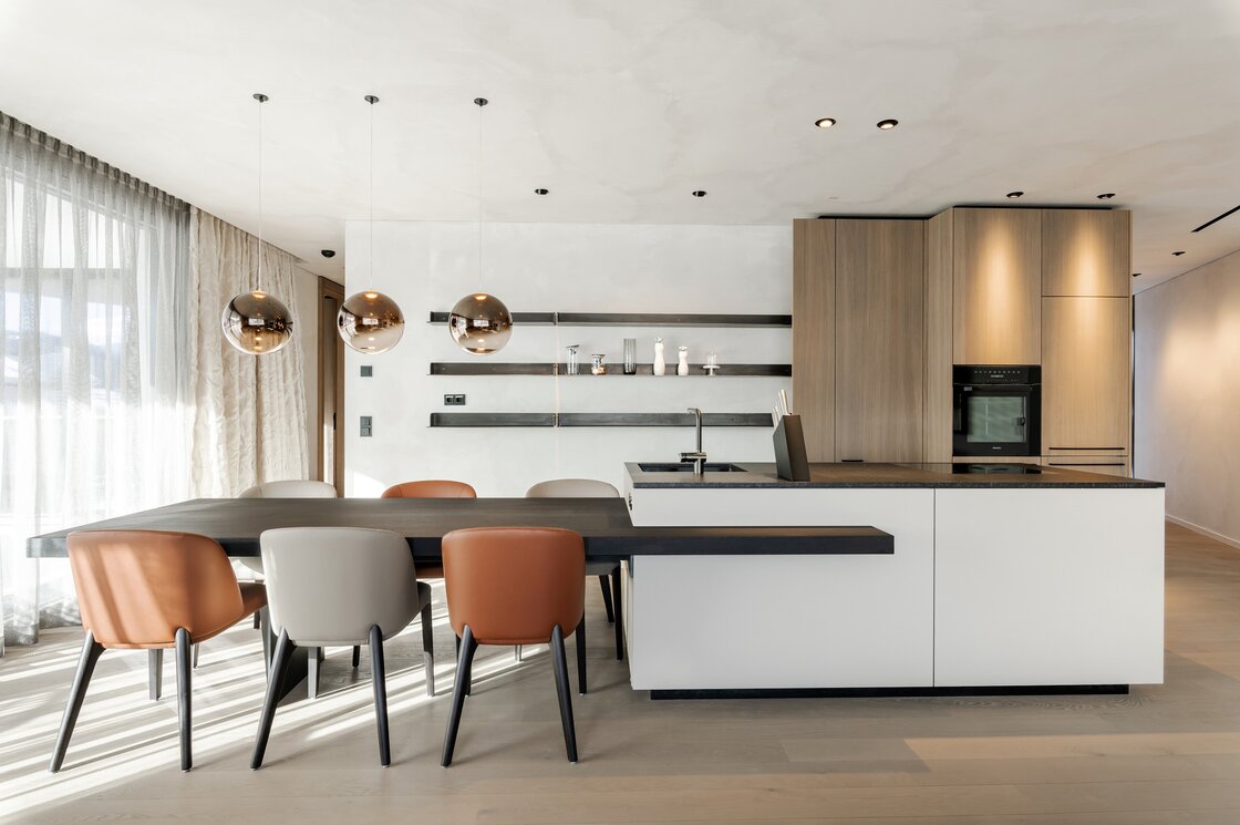 Luxuriöse Apartmentküche mit Essbereich in Fiss Helle Apartmentküche mit großem Esstisch, Designstühlen und Kochinsel mit Holzfronten.