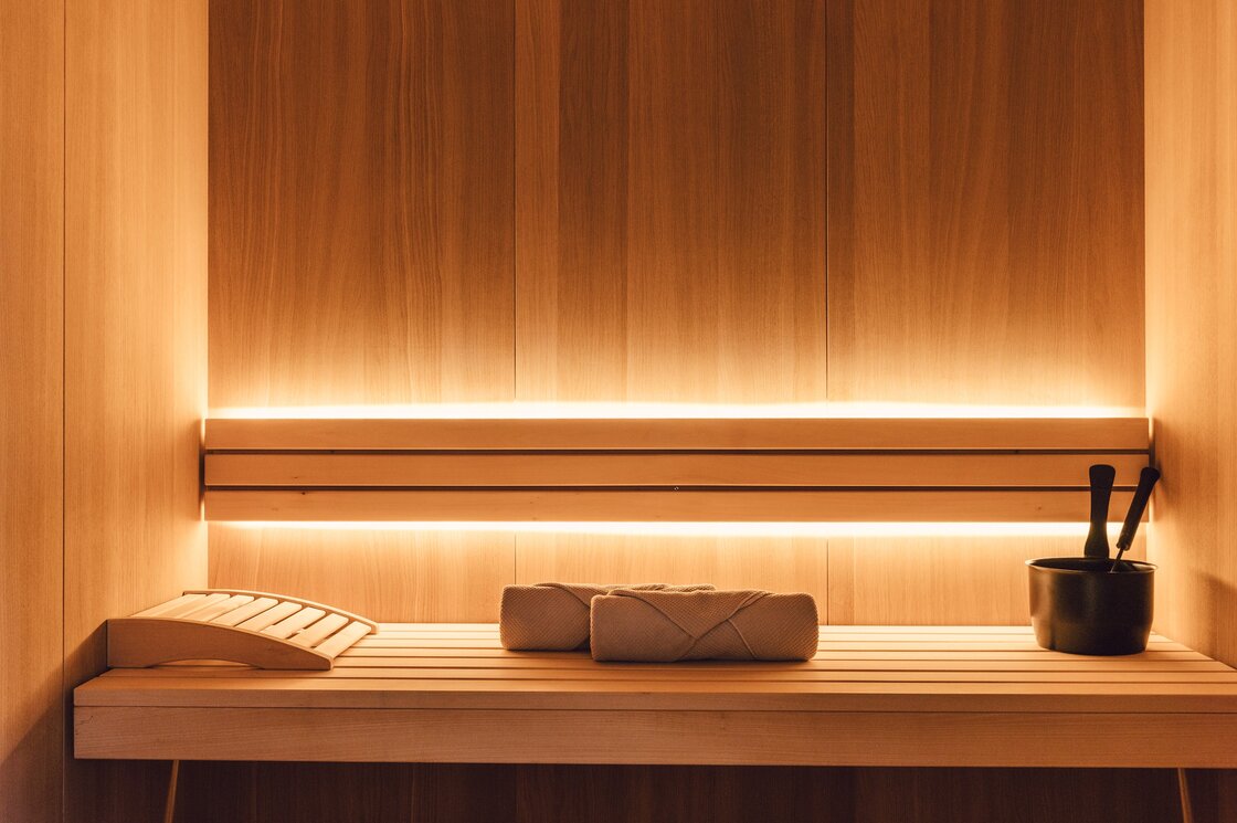 Private Sauna im Apartment in Fiss Warme Holzwand in einer privaten Sauna mit Liegebank, Handtüchern und Aufgusseimer.
