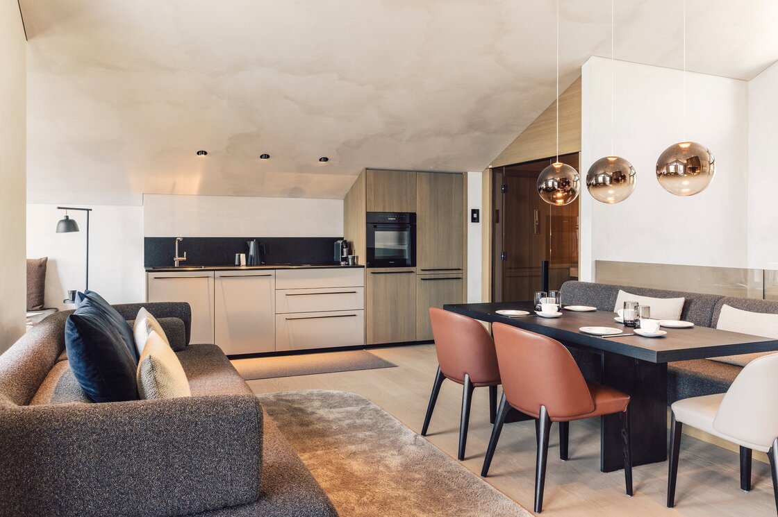 Penthouse-Wohnbereich mit Küche in Fiss Der Wohnbereich eines modernen Penthouses mit Küchenzeile, Esstisch und Sofa unter einer schrägen Decke.