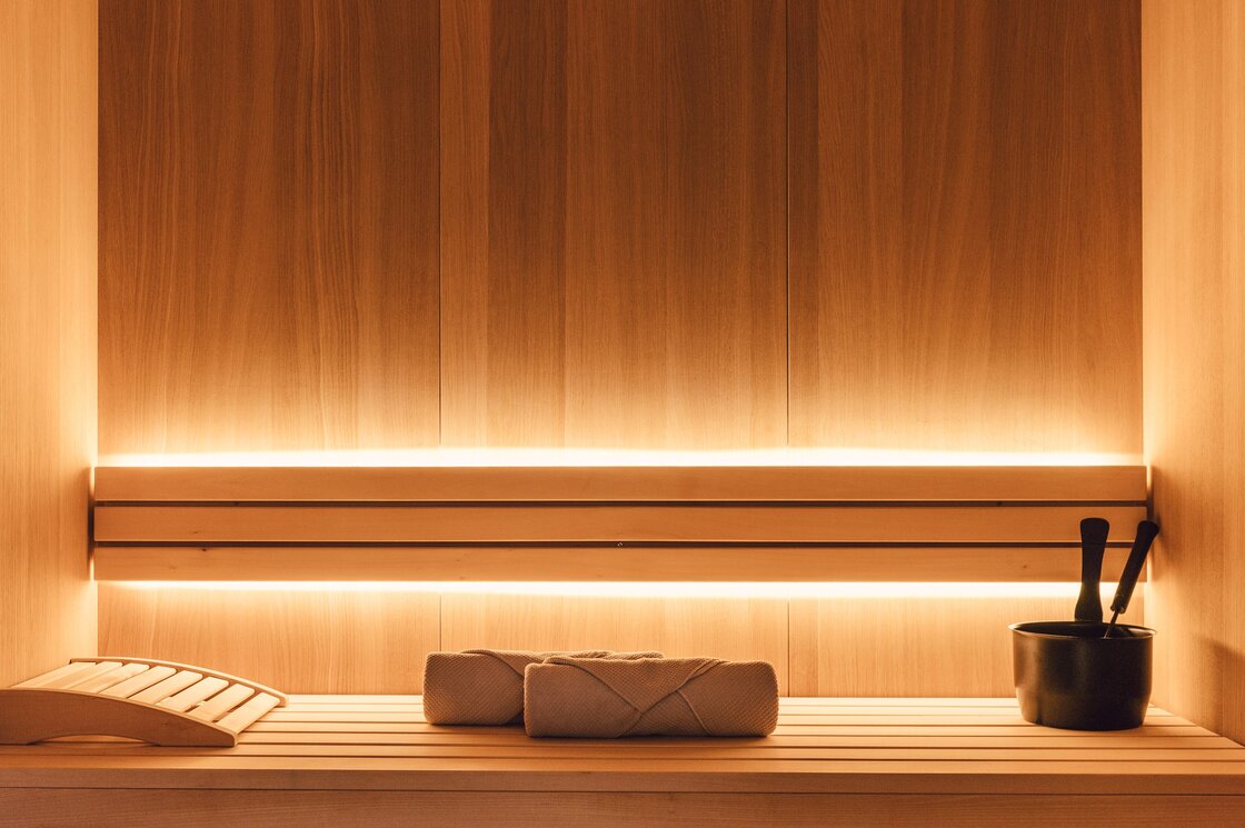 Private Sauna im Luxury Apartment in Fiss Eine Holzsauna mit Liegen und Aufgusseimer, warm beleuchtet im Apartment.