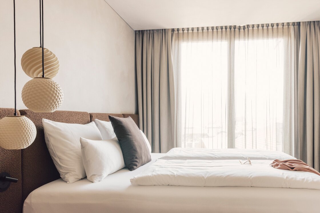 Elegantes Schlafzimmer im Luxury Apartment Fiss Ein modern eingerichtetes Schlafzimmer mit Doppelbett, großen Kissen und lichtdurchlässigen Vorhängen vor dem Fenster.