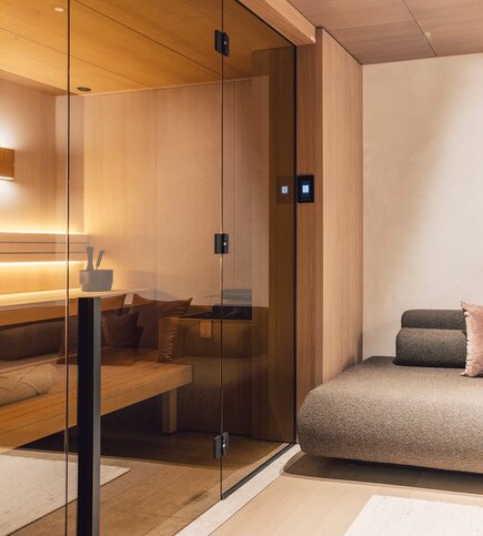 Private Sauna in the Apartment in Fiss A modern private sauna with wood paneling and a glass front beside a cushioned lounger.