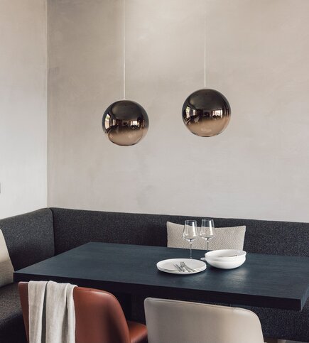 Design-Essbereich im Apartment in Fiss Ein moderner Essbereich im Apartment mit dunkler Bank, Tisch und zwei Pendelleuchten.