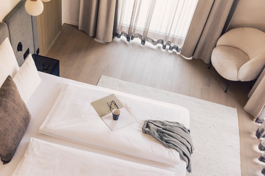 Helles Schlafzimmer im Penthouse mit Bergblick Ein helles Schlafzimmer mit Doppelbett, Sessel und großen Fenstern mit Vorhängen.