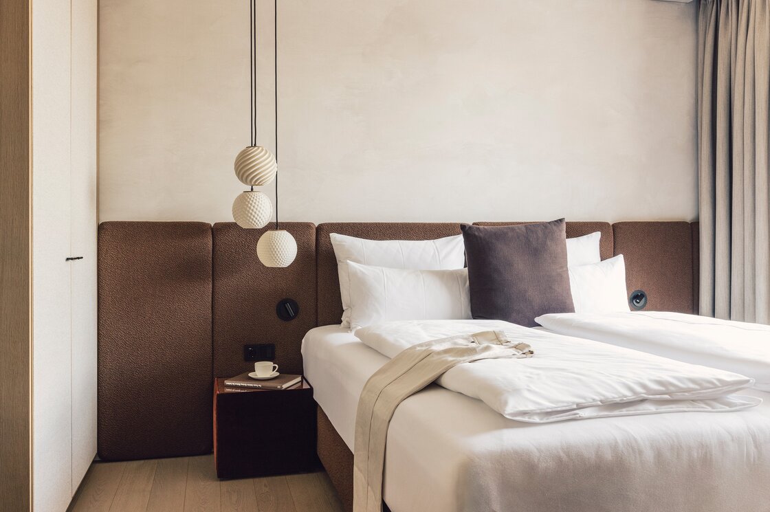 Doppelbett im Luxury Apartment in Fiss Ein stilvoll bezogenes Doppelbett mit braunem Kopfteil und hängenden Lampen in einem hellen Schlafzimmer.
