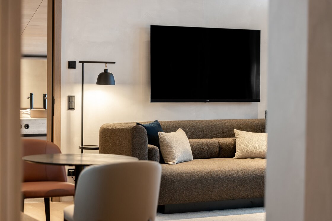 Penthouse-Wohnbereich mit Sofa und TV Ein moderner Wohnbereich mit Sofa, Stehleuchte und großem Wandfernseher.