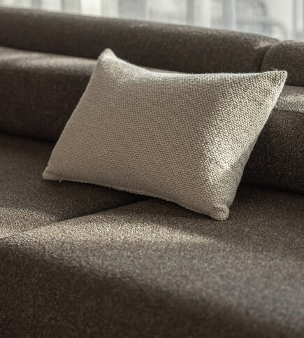 Textilkissen auf braunem Sofa Ein helles Textilkissen liegt auf einem braunen Sofa im weichen Tageslicht.