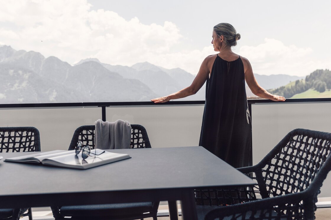 Apartment mit Balkon und Bergblick in Fiss Eine Frau steht auf dem Balkon und blickt auf die Berge, vor ihr stehen ein Tisch und Stühle.